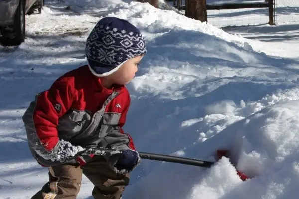 Young boy in a red jacket and winter hat shoveling snow