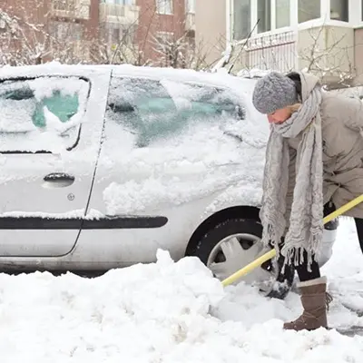 Woman in a hat, jacket, and scarf shoveling snow